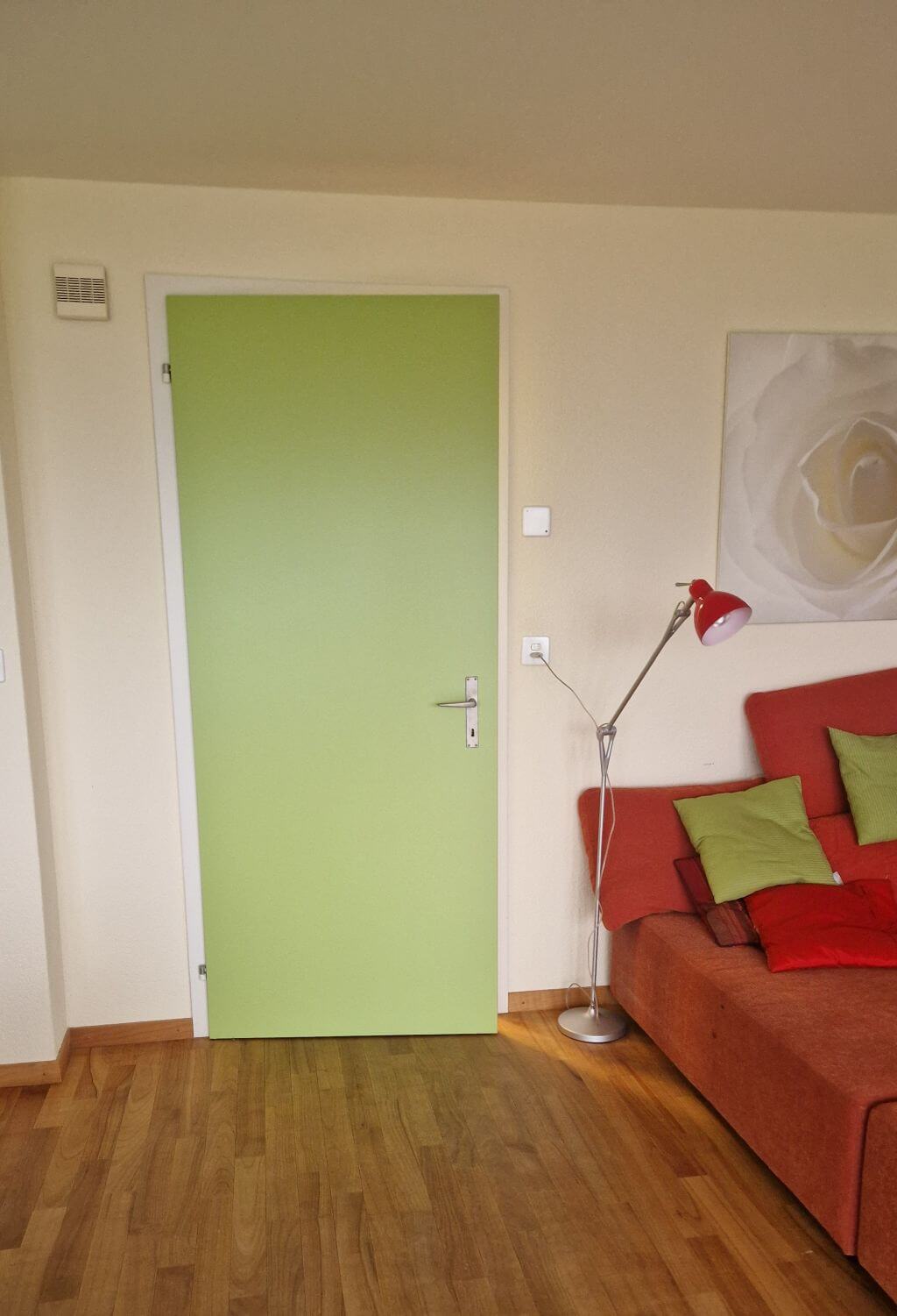 Farbige Tür in Hellgrün mit hellem Wandbereich und rotem Sofa im Wohnraum