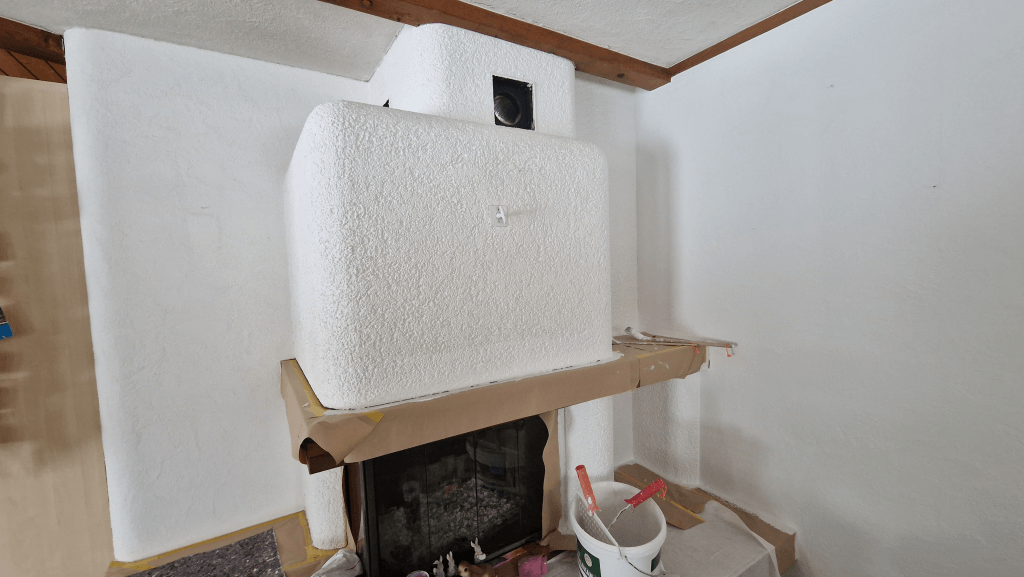 Renovationsarbeiten an einem Kaminbereich mit frisch gestrichenen Wandflächen und abgedecktem Boden.