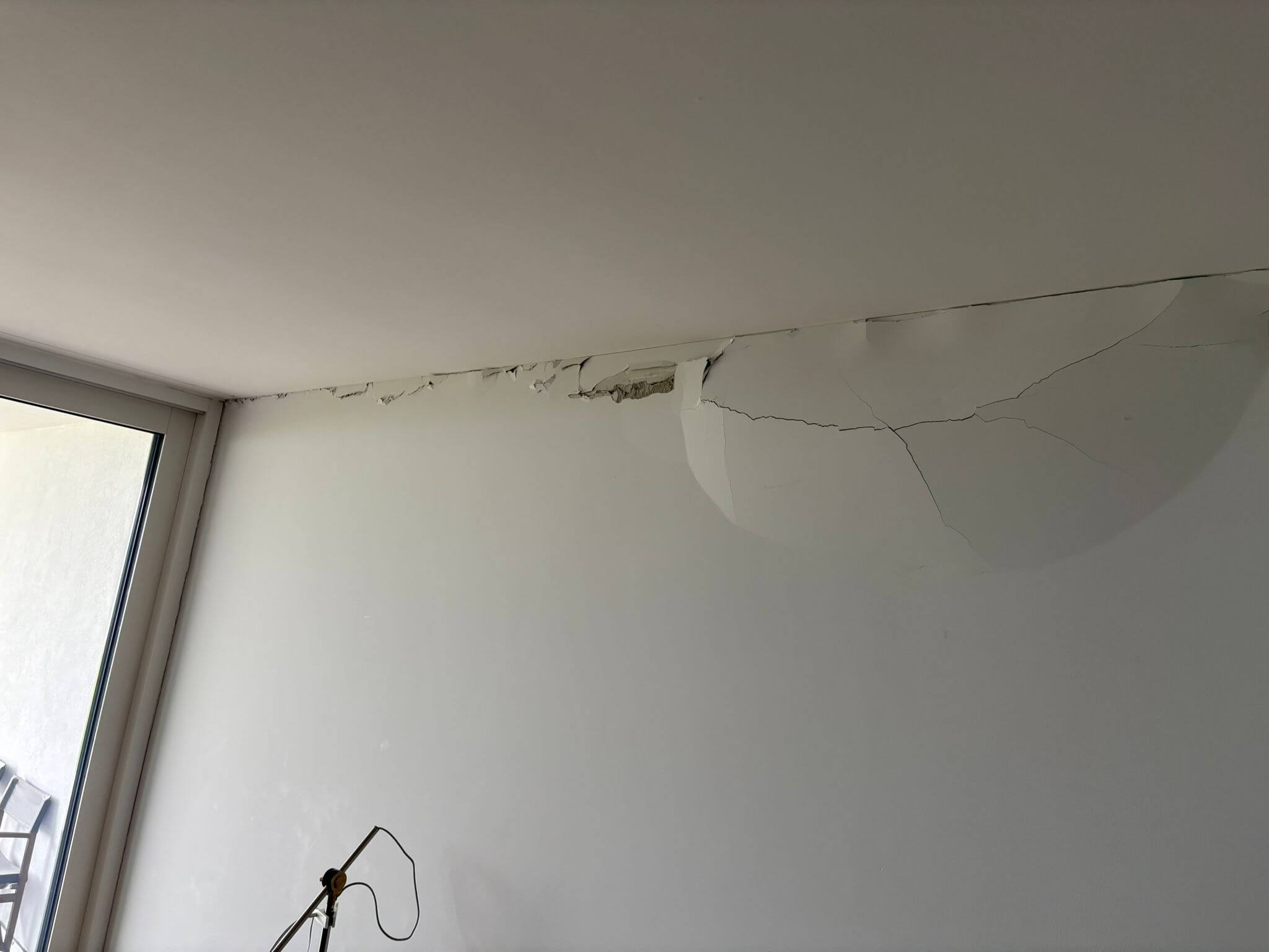 Beschädigte Wand und Decke mit Rissen und abblätternder Beschichtung vor der Renovation.