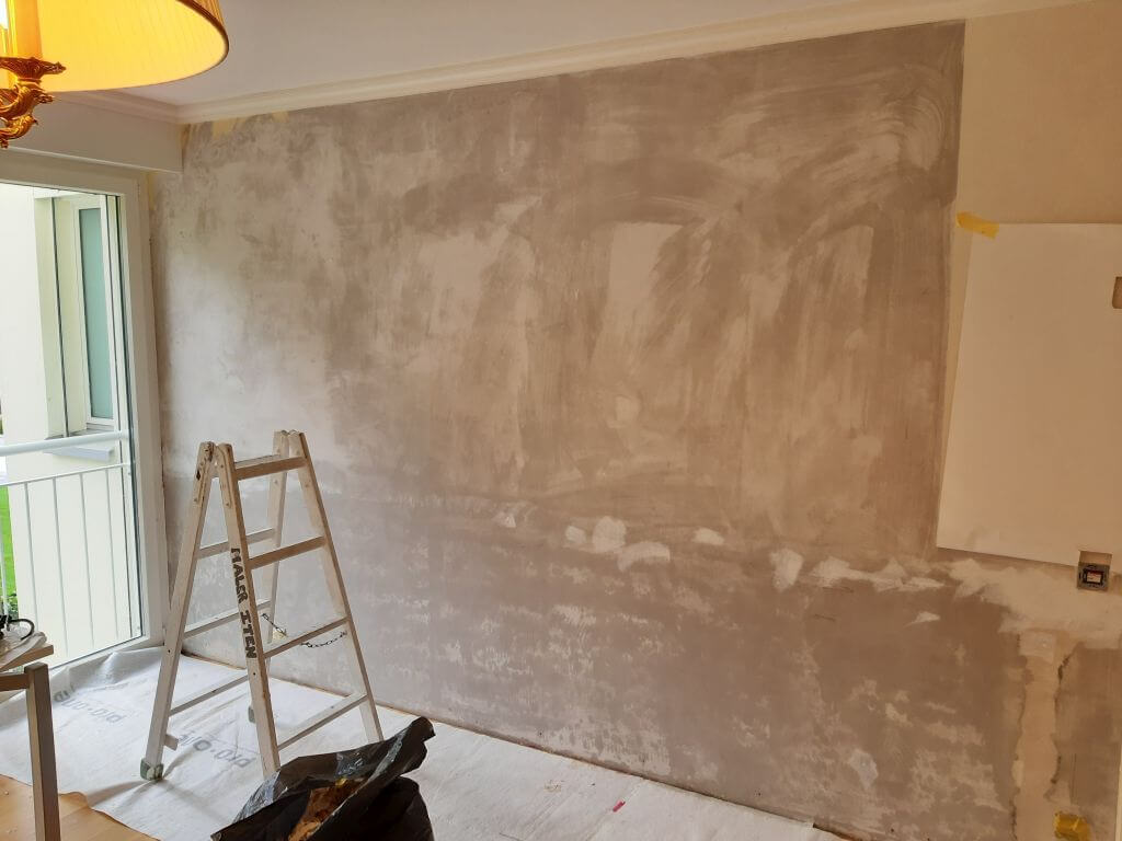Vorbereitete Wand für Tapezierarbeiten in einem Wohnraum mit Leiter und geschütztem Boden.